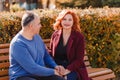 A smiling middle-aged woman and a man hold hands while sitting on a park bench in the fall Royalty Free Stock Photo