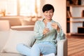 Smiling middle aged woman scrolling through app on cellphone indoor