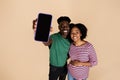 Smiling millennial african american guy and woman with big belly show phone with blank screen