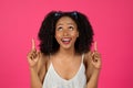 Smiling millennial african american lady showing fingers up on empty space isolated on pink background, studio