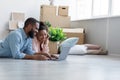 Smiling millennial african american male and female lies on floor in new apartment among boxes, planning interior