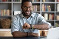 Smiling millennial african american man checking time on wristwatch.