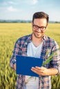Smiling millennial agronomist or farmer inspecting wheat field before the harvest, writing data to a clipboard Royalty Free Stock Photo