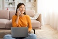Smiling millennial asian lady using laptop and speaking on smartphone Royalty Free Stock Photo