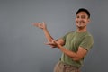 Smiling Asian man open his palms on an empty space on isolated grey background Royalty Free Stock Photo