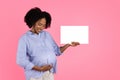 Smiling millennial black pregnant mom with big belly shows banner with free space, enjoy expect baby