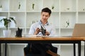 Smiling millennial businessman sitting at his desk in a bright modern office and using laptop Royalty Free Stock Photo