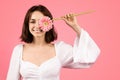 Smiling millennial caucasian brunette woman puts flower to eye, has fun