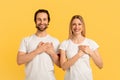 Smiling millennial caucasian family in white t-shirts press their hands to chest, isolated on yellow background Royalty Free Stock Photo