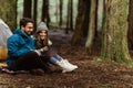 Smiling millennial caucasian guy and woman hikers in jackets relaxing in cold forest, enjoy adventure