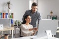 Smiling millennial european female showing to man manager with hand in computer screen Royalty Free Stock Photo