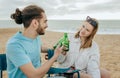Smiling millennial european lady and arab guy in casual cheers bottles of beer, enjoy weekend on beach