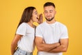 Smiling millennial european woman in white t-shirt whispers secrets in ear of confident guy