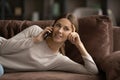 Smiling millennial female lying on comfy sofa talking on telephone