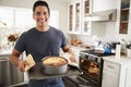 Smiling millennial Hispanic man standing in kitchen presenting the cake he has baked to camera