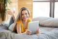 Smiling millennial woman using tablet computer for online work or education on bed at home, blank space Royalty Free Stock Photo