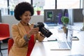 Smiling mixed race businesswoman sitting at desk using camera in creative office Royalty Free Stock Photo