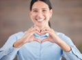 Smiling mixed race businesswoman standing alone and using hand gestures to make a heart shape. Confident and ambitious