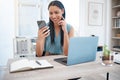 Smiling mixed race businesswoman using smartphone and working on a laptop at her desk. One confident female entrepreneur Royalty Free Stock Photo