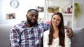 Smiling mixed-race couple sitting on sofa at home and looking at camera, family Royalty Free Stock Photo