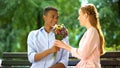 Smiling mixed-race teen boy presenting beloved girl flowers, first date in park