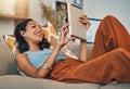 Smiling mixed race woman browsing internet on digital tablet at home. Happy hispanic lying down on living room sofa Royalty Free Stock Photo
