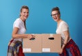 Smiling modern female roommates with cardboard boxes on blue