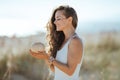 Smiling modern woman on ocean shore holding coconut