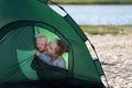 Smiling mom and baby peeking out of tourist tent. Tent on the sandy beach. Camping