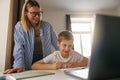 Little smiling schoolboy using laptop to do school homework with help of his mom Royalty Free Stock Photo