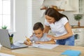 Smiling mom is helping her son doing homework while he is studying online using laptop. Royalty Free Stock Photo