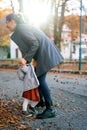 Smiling mom holding hands a little girl hiding her face in her lap while standing under falling leaves Royalty Free Stock Photo