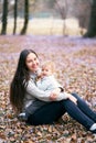 Smiling mom holding a laughing baby in her arms sitting on the grass among small wildflowers in the park