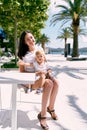 Smiling mom holds on her lap a little girl sitting on a chair in a cafe on the beach Royalty Free Stock Photo