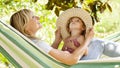 Smiling mom and little girl daughter child blue eyes with blond curly hair, together lying on the hammock in the green home garden Royalty Free Stock Photo