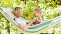 Smiling mom and little girl daughter child blue eyes with blond curly hair, together lying on the hammock in the green home garden