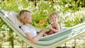 Smiling mom and little girl daughter child blue eyes with blond curly hair, together lying on the hammock in the green home garden Royalty Free Stock Photo