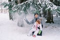 Smiling mom with a little girl sits on her knees in the snow under snowfall from pine branches Royalty Free Stock Photo