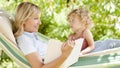 Smiling mom reading a story from the book to the little girl daughter child blue eyes with blond curly hair, together lying on the Royalty Free Stock Photo