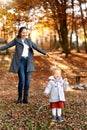 Smiling mom throws up fallen leaves over a little laughing girl in an autumn park Royalty Free Stock Photo