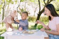 Smiling mom with toy cup in hand watches little girl giving tea to teddy bear at table in garden Royalty Free Stock Photo