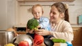 Smiling mother with baby boy playing and singing songs with vegetables and fruits on kitchen. Concept of little chef, children Royalty Free Stock Photo