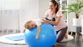 Smiling mother and baby doing fitness exercises on fitball at home. Concept of child healthcare, kids sports and yoga Royalty Free Stock Photo