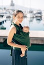 Smiling mother with a baby in a sling on the background of yachts. Close-up Royalty Free Stock Photo