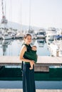 Smiling mother with a baby in a sling stands on the pier on the background of yachts Royalty Free Stock Photo