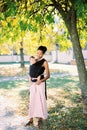 Smiling mother with a baby in a sling stands under a tree Royalty Free Stock Photo