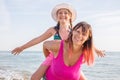 Smiling mother and beautiful daughter having fun on the beach. Portrait of happy woman giving a piggyback ride to her girl Royalty Free Stock Photo