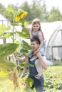 Smiling mother carrying daughter on shoulders by sunflower plant at farm