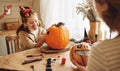 Smiling mother and child girl drawing scary faces on Halloween pumpkins while sitting in cozy kitchen Royalty Free Stock Photo
