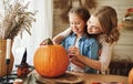 Smiling mother and child girl drawing scary faces on Halloween pumpkins while sitting in cozy kitchen